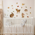 A collection of forest woodland wall decals including animals like deer and squirrels, as well as butterflies and leaves, applied on a wall above a white crib.